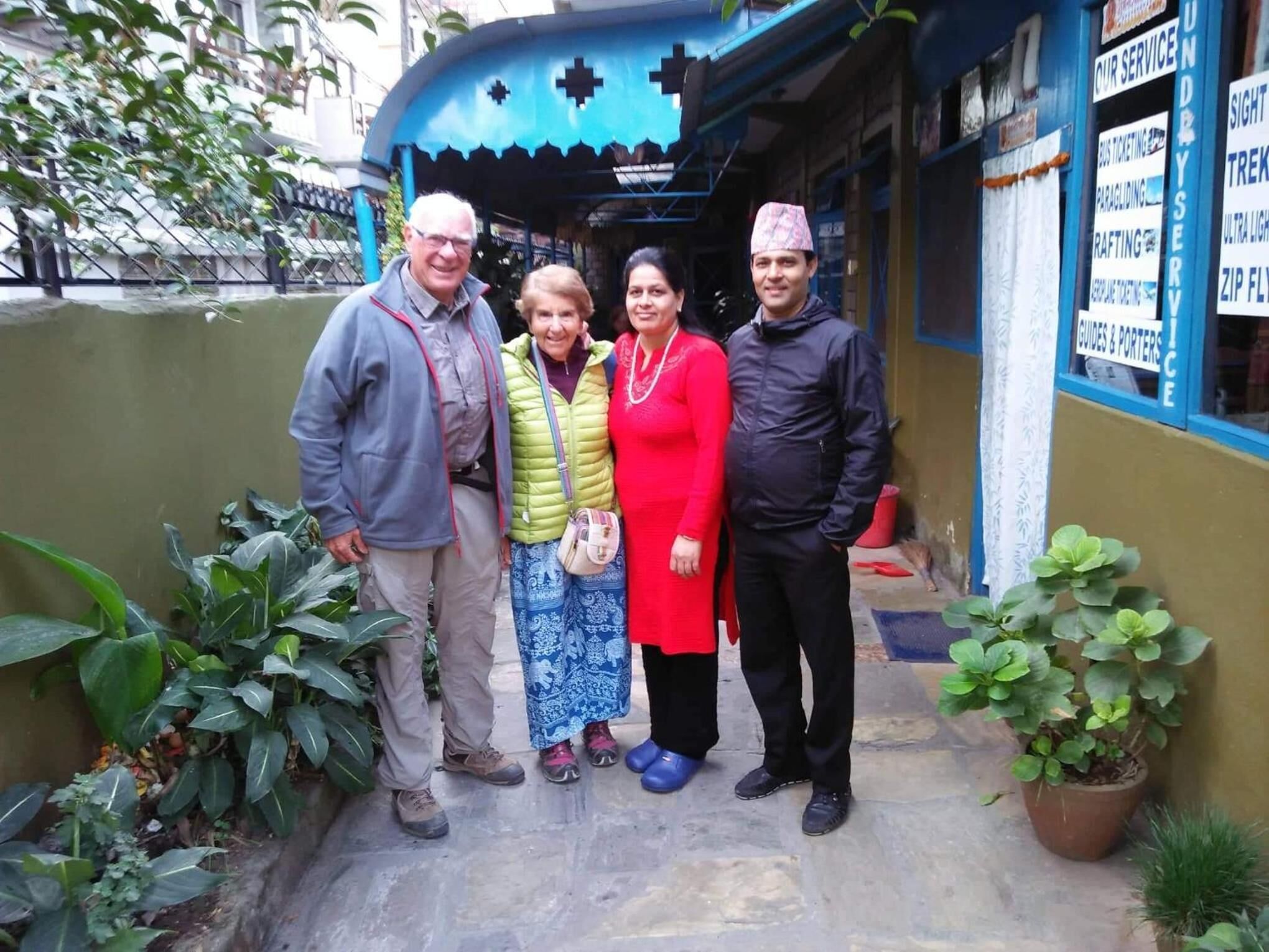 A group of people standing in front of a building with a blue awning and a signboard listing services like trekking and zip flying.
