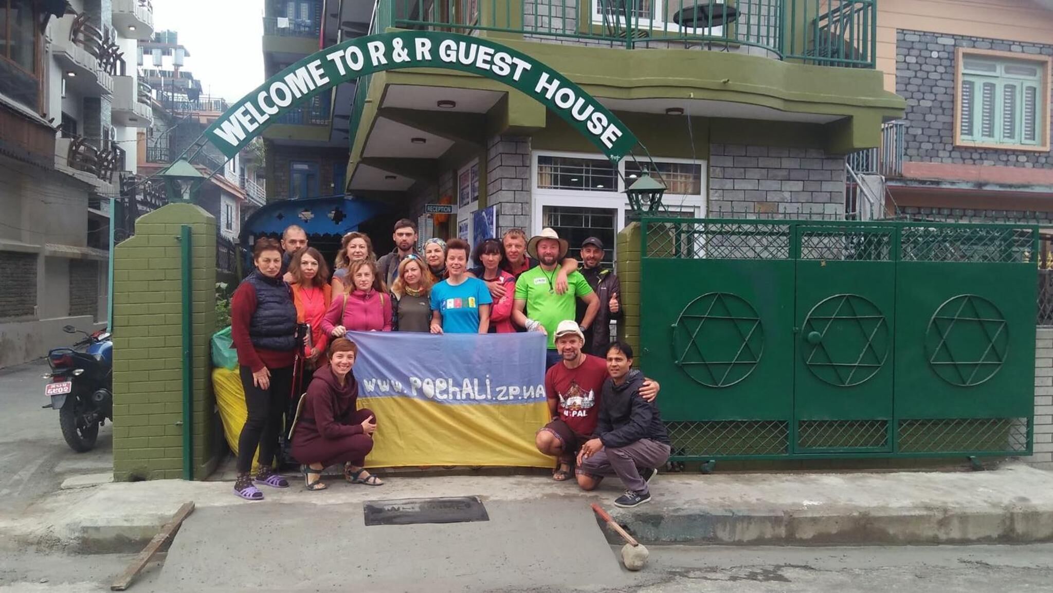 A group of people posing in front of a building with a sign that reads "WELCOME TO R & GUEST HOUSE".