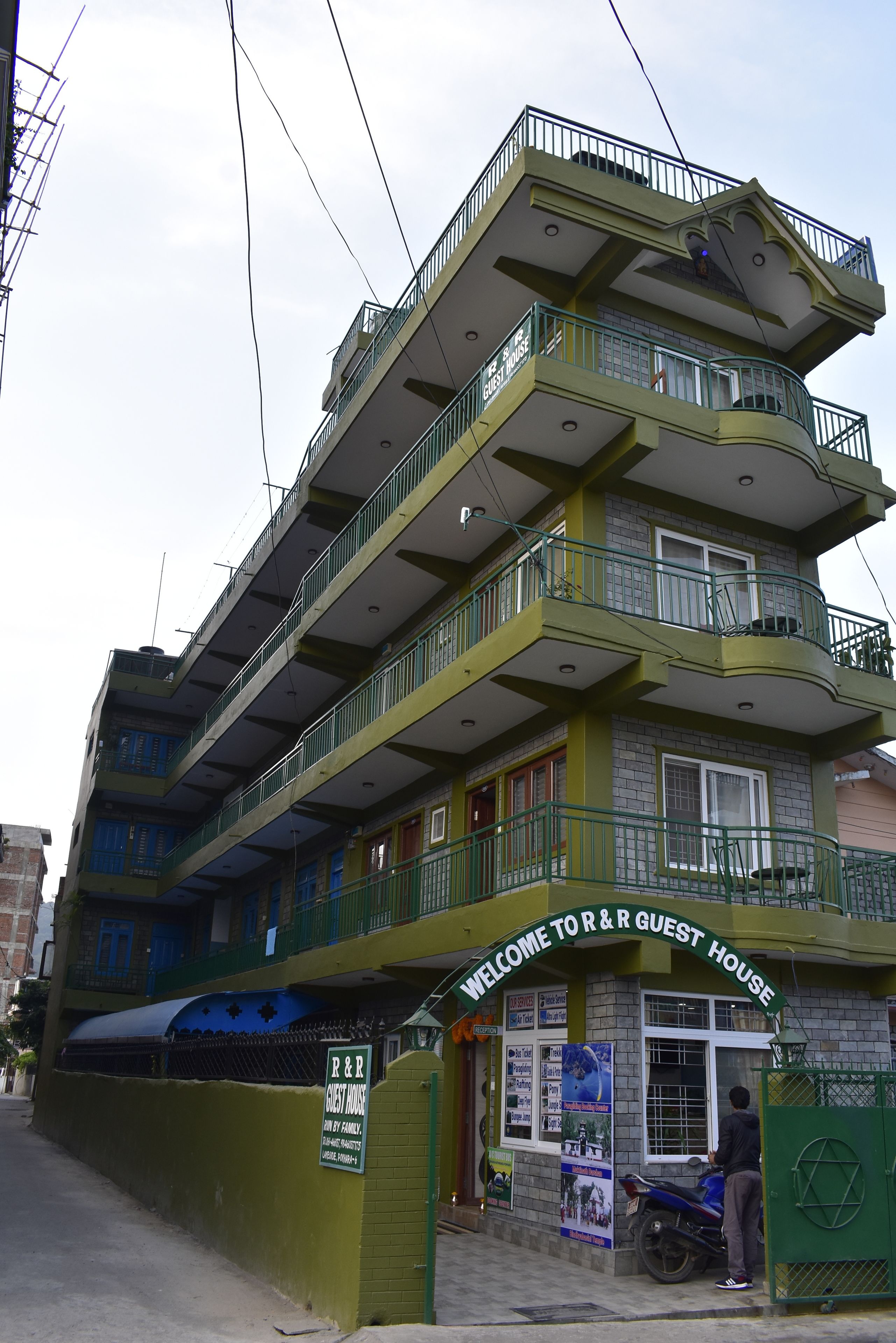 A multi-story guest house with balconies and a sign reading "Welcome to R&R Guest House."