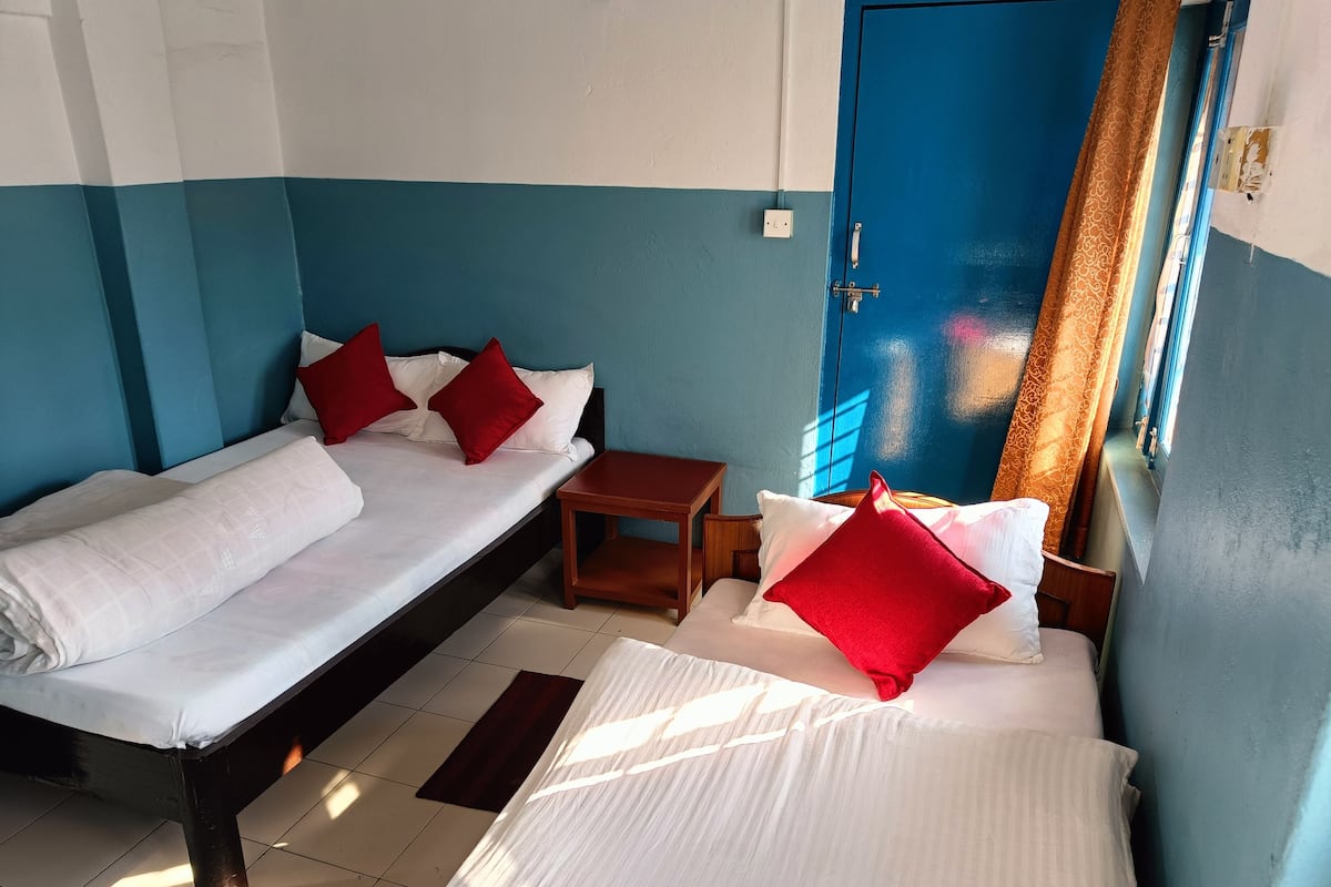 A room with two beds, each with white linens and red pillows, a small wooden table, and a blue door.