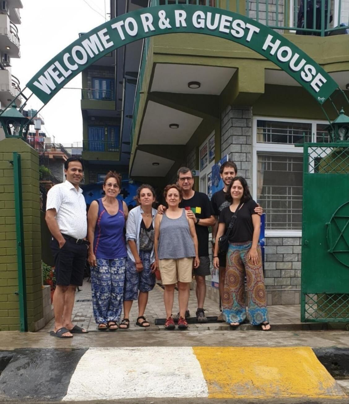 A group of people standing in front of a building with a sign that reads "WELCOME TO R&R GUEST HOUSE".