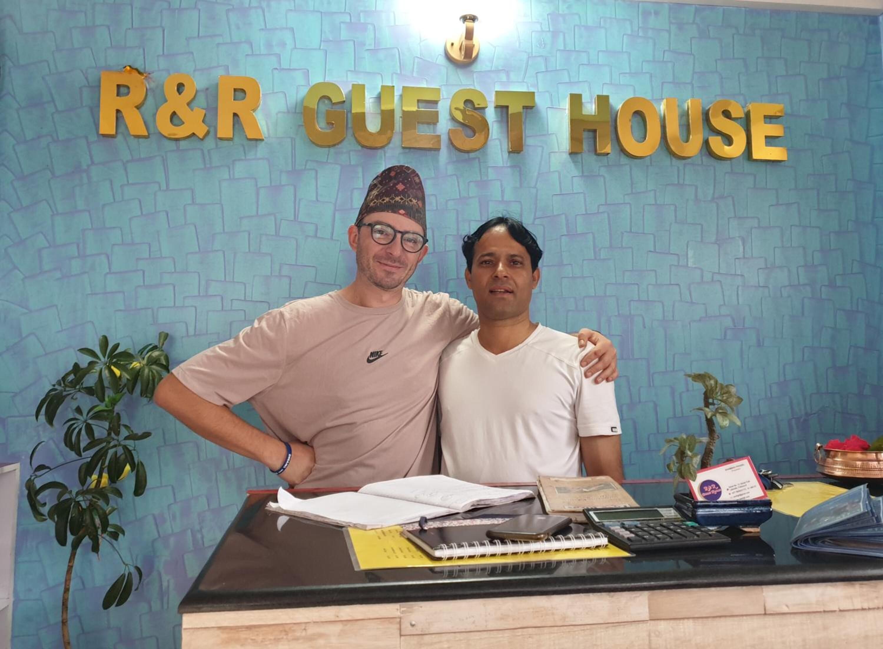 Una mesa de recepción con un letrero que dice "R&R Guest House" y una pared con un estampado azul.