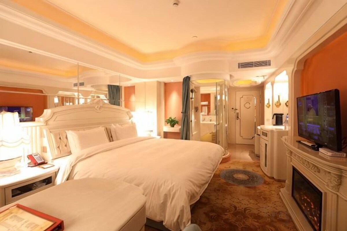 A hotel room with a large bed, a television, a fireplace, and a bathroom visible through an open door.
