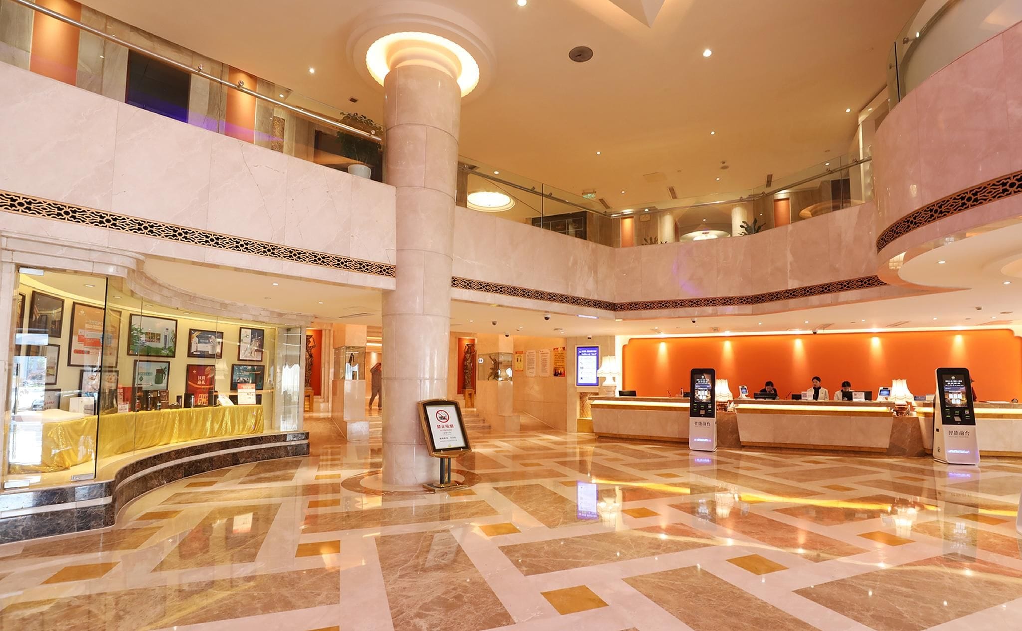 A hotel lobby with a reception desk, a glass storefront, and a high ceiling with a central column.