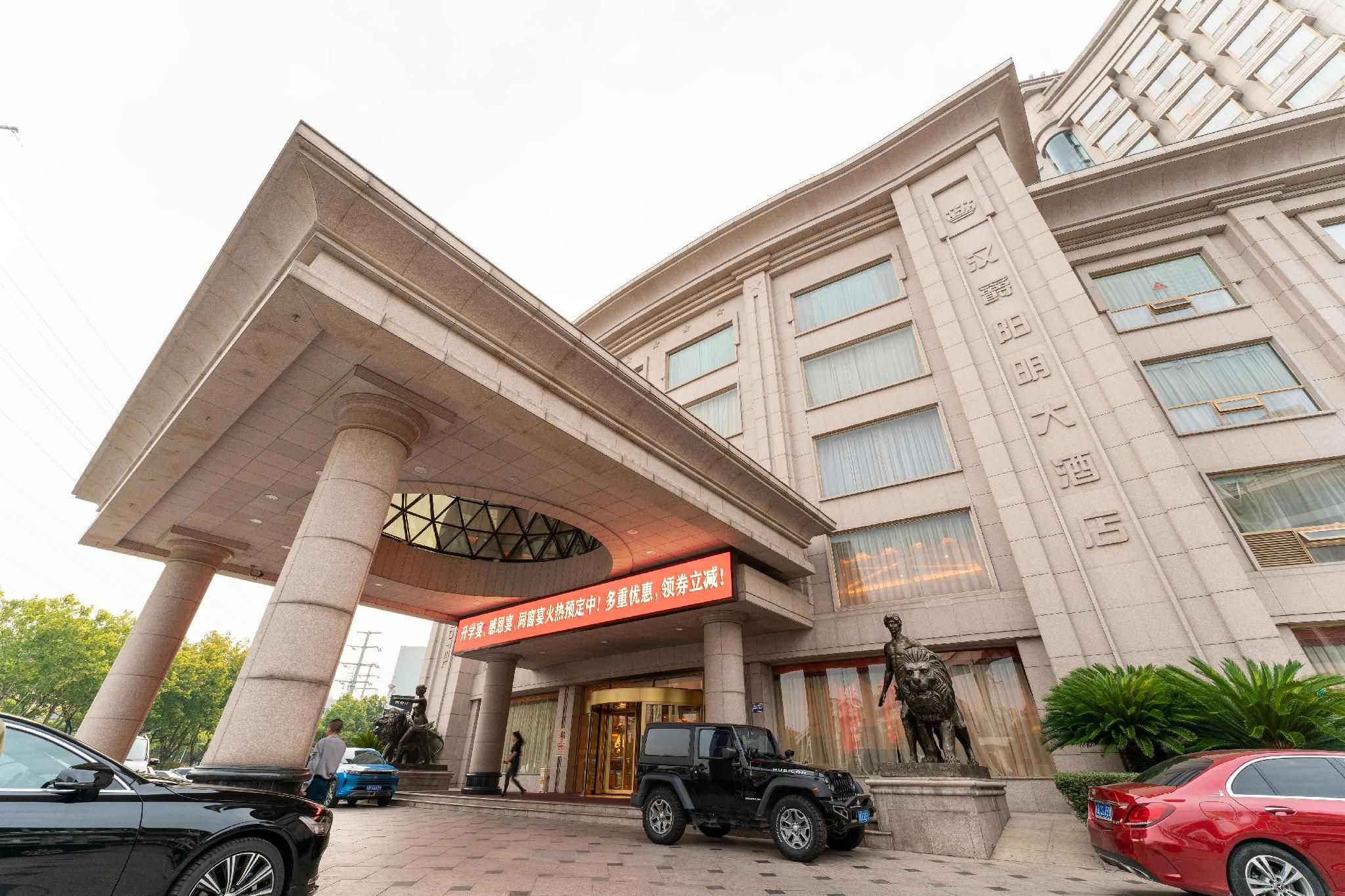 A hotel entrance with a large archway, a statue, and a red sign.
