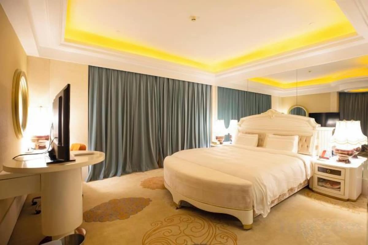 A hotel room with a large bed, bedside tables, a TV, and a mirror.