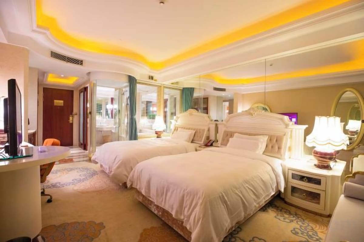 A hotel room with two beds, a desk, a chair, a mirror, and a lamp.