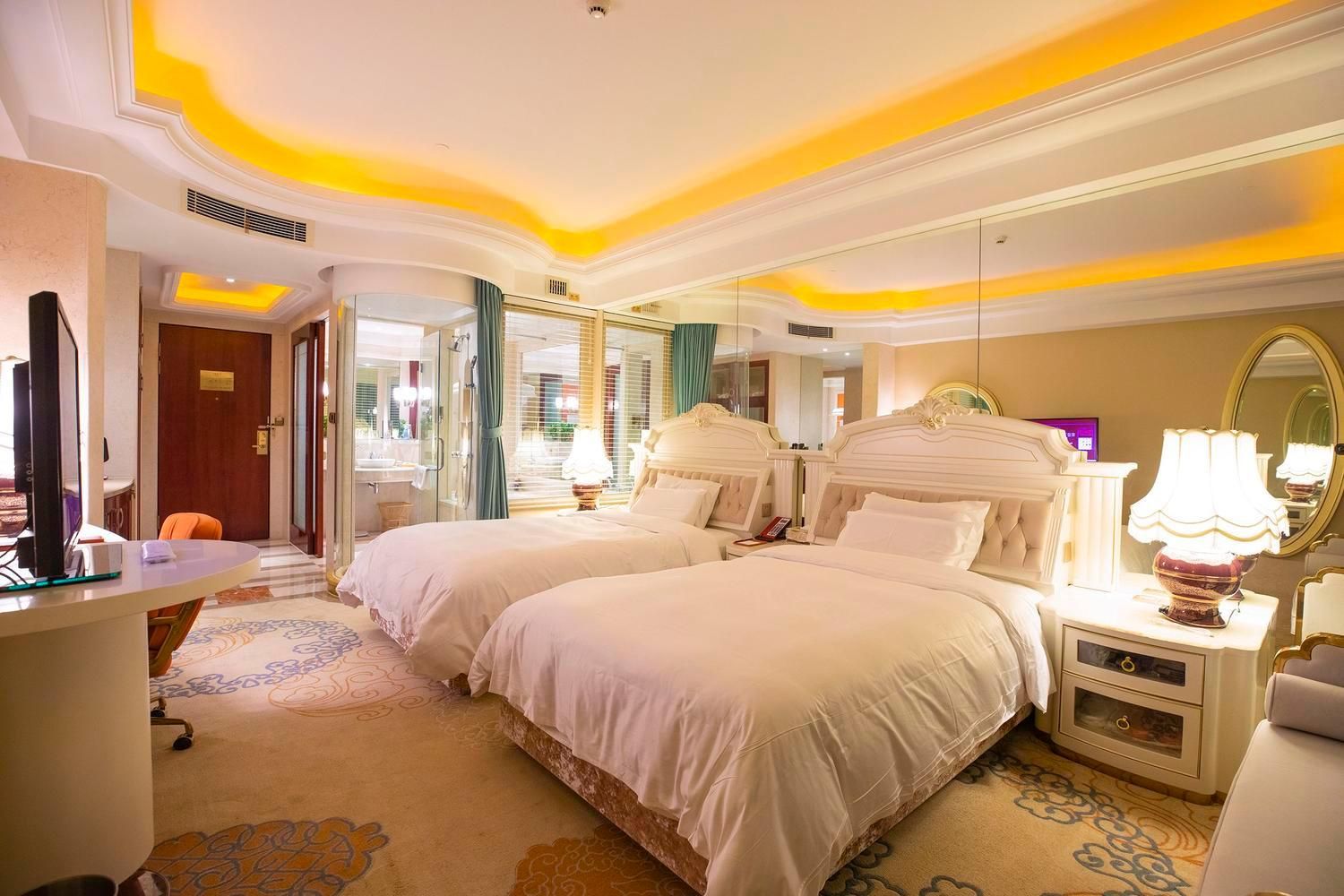 Une chambre d’hôtel avec deux lits, un bureau, un miroir et une salle de bain visible à travers une porte en verre.