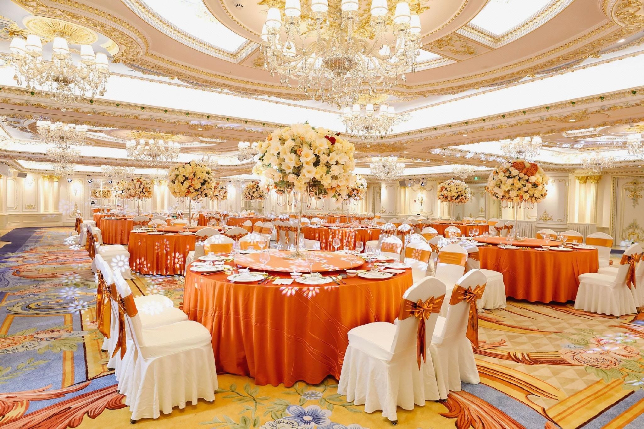 A banquet hall with round tables, white chairs, and floral centerpieces.