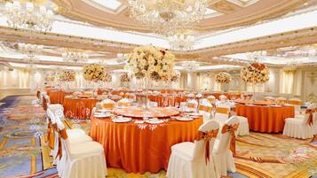 A banquet hall with round tables, white chairs, and floral centerpieces.