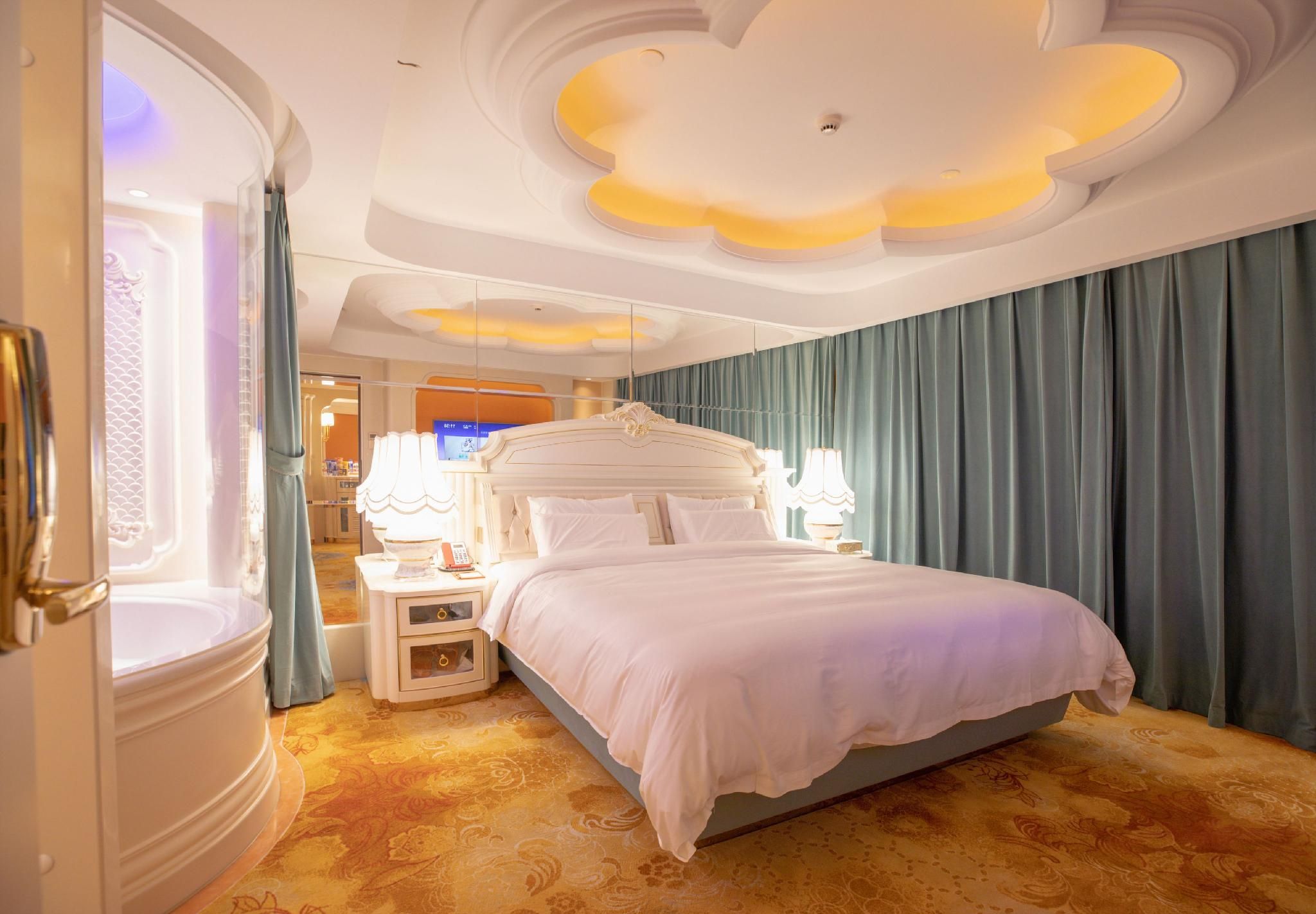 A hotel room with a large bed, a bedside table with a lamp, a mirror, and a bathroom with a bathtub.