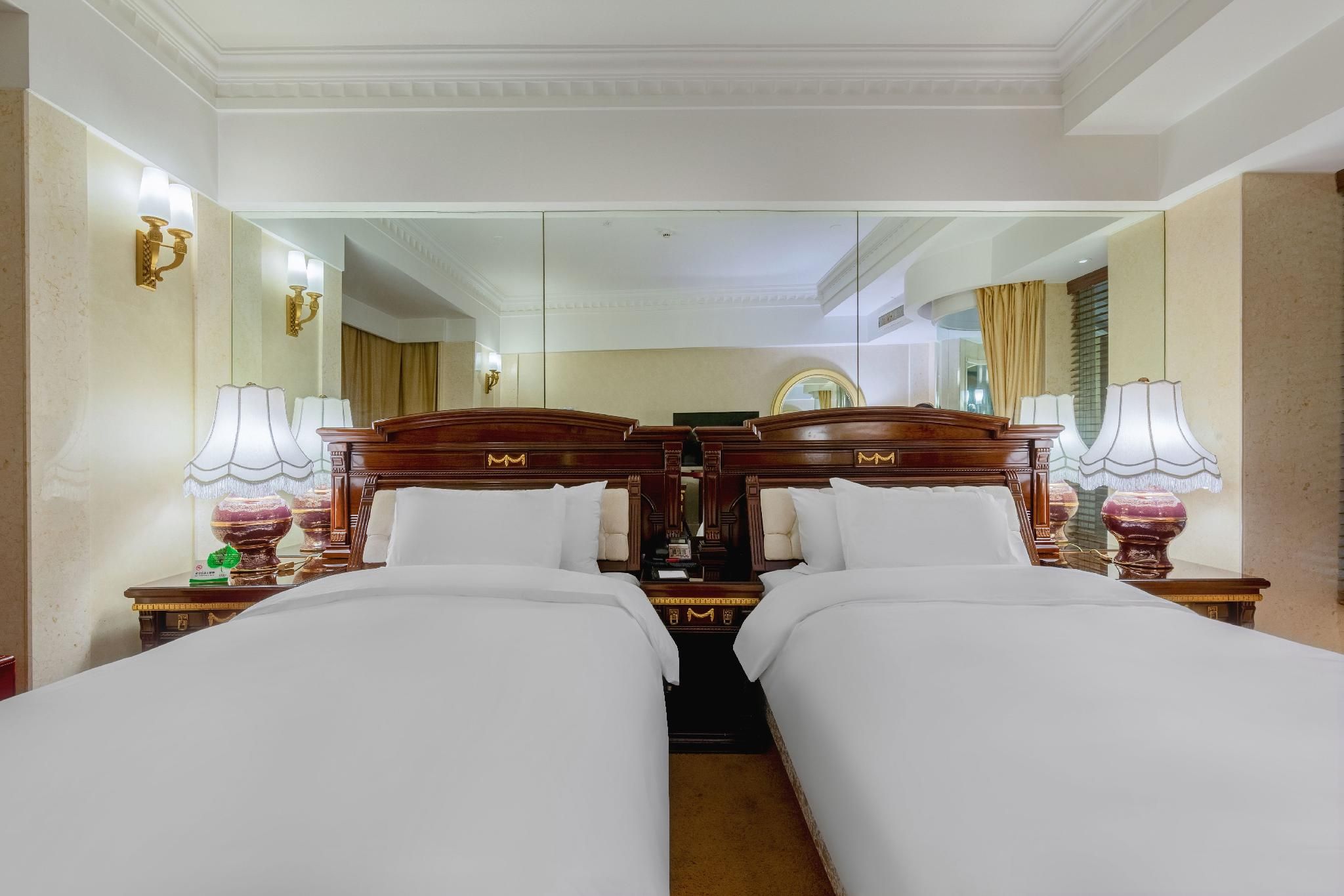 A hotel room with two beds, a large mirror, and a chandelier.