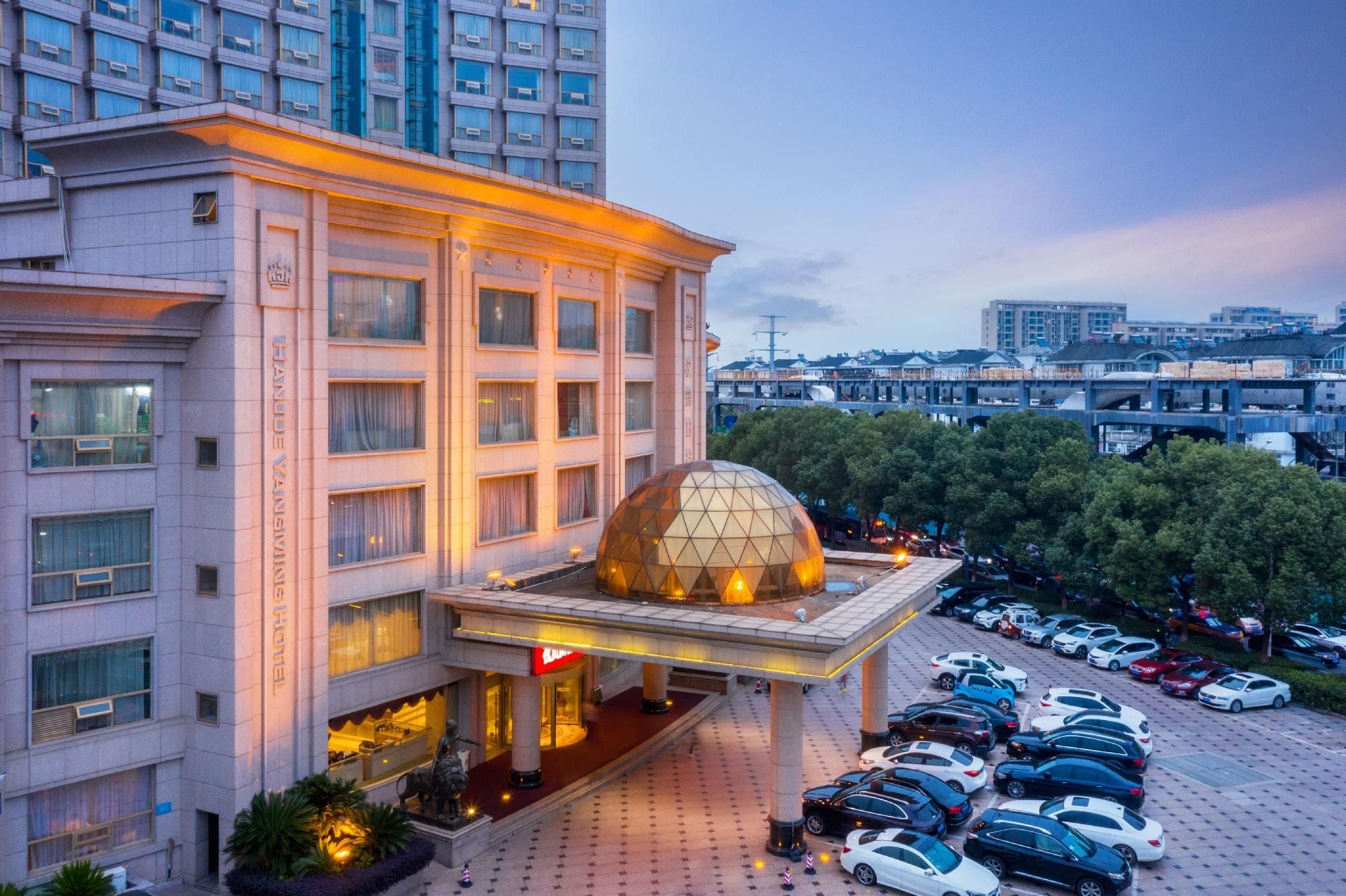 A hotel with a prominent dome structure, multiple floors, and a parking area with cars.
