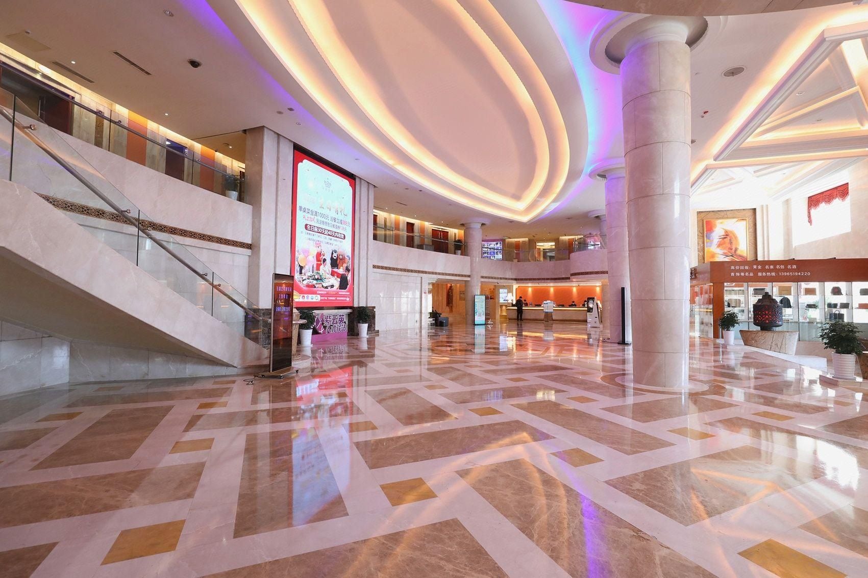 A spacious lobby with a marble floor, a staircase, and a reception desk.
