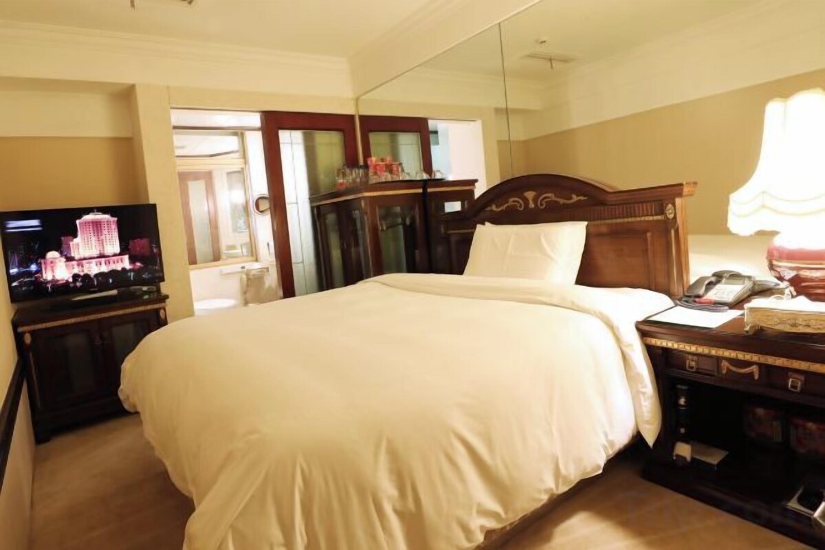 A hotel room with a large bed, a television, a desk with a telephone, and a mirror.