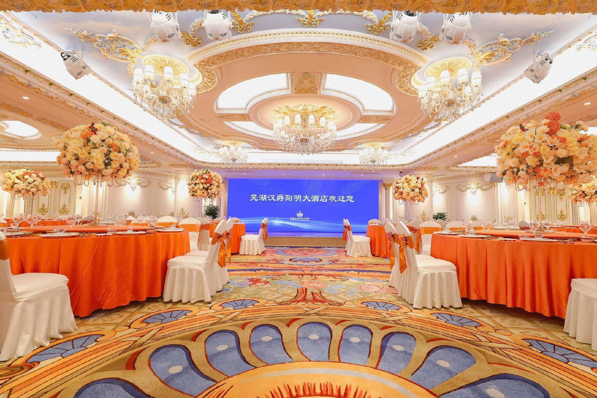 Un salón de banquetes con mesas redondas, sillas blancas y centros de mesa florales.