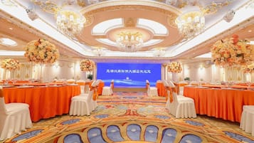 Un salón de banquetes con mesas redondas, sillas blancas y centros de mesa florales.