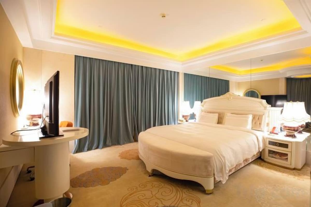 A hotel room with a large bed, bedside tables, a TV, and a mirror.