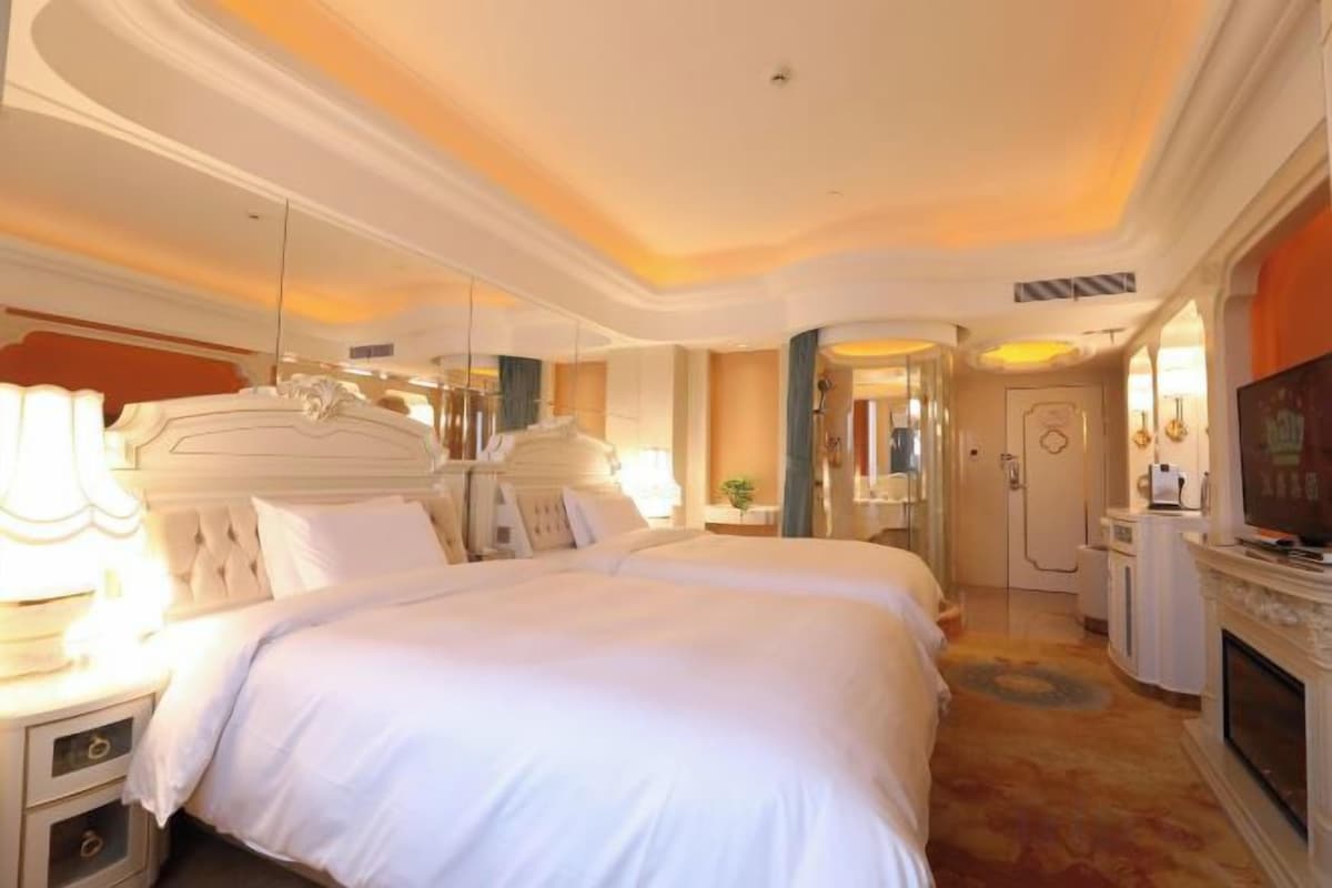 A hotel room with a large bed, bedside tables, a television, and a fireplace.