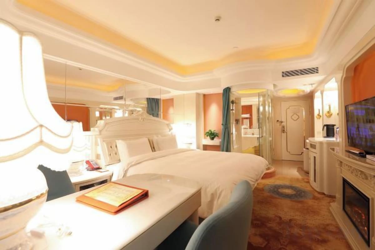 A hotel room with a bed, bedside table, lamp, television, and a fireplace.
