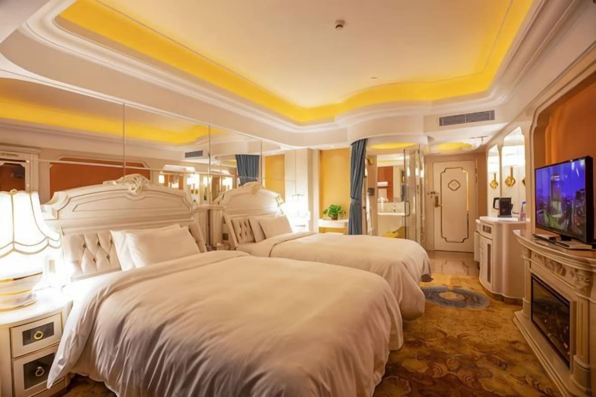 A hotel room with two beds, a television, a fireplace, and a mirror.