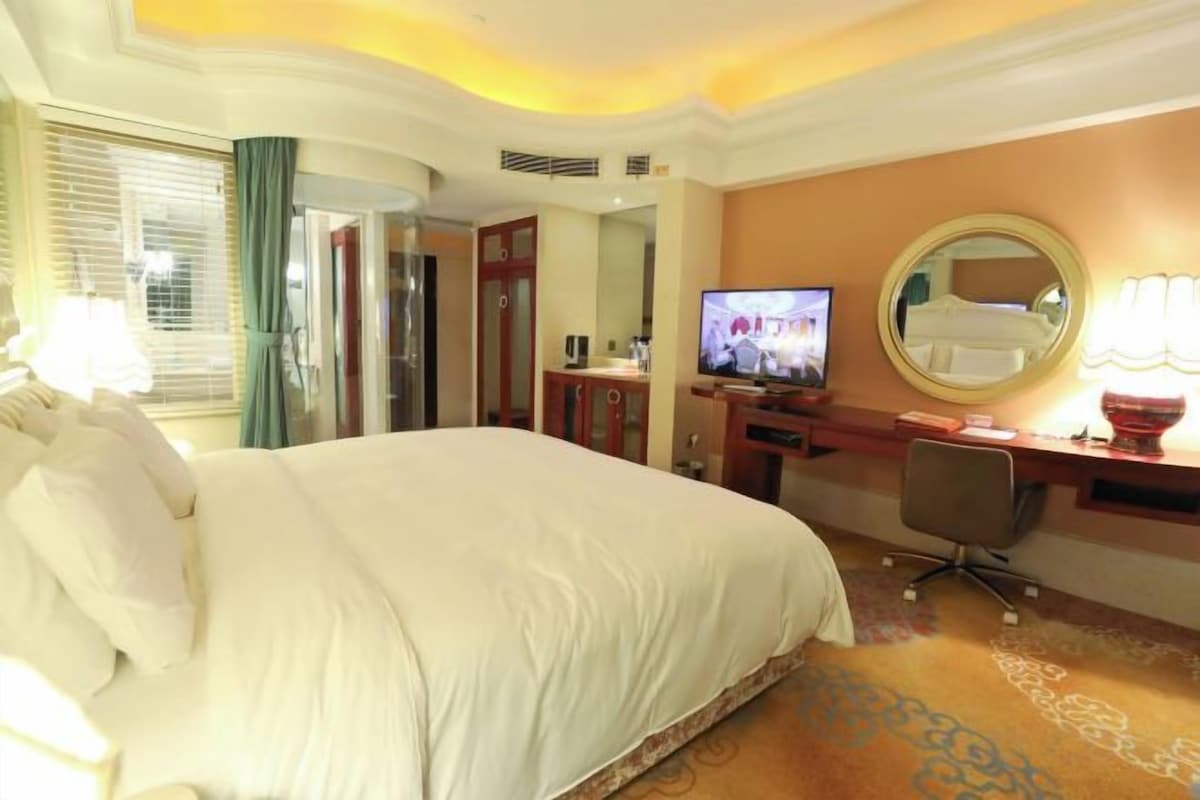 A hotel room with a large bed, a desk with a computer, a television, and a mirror.