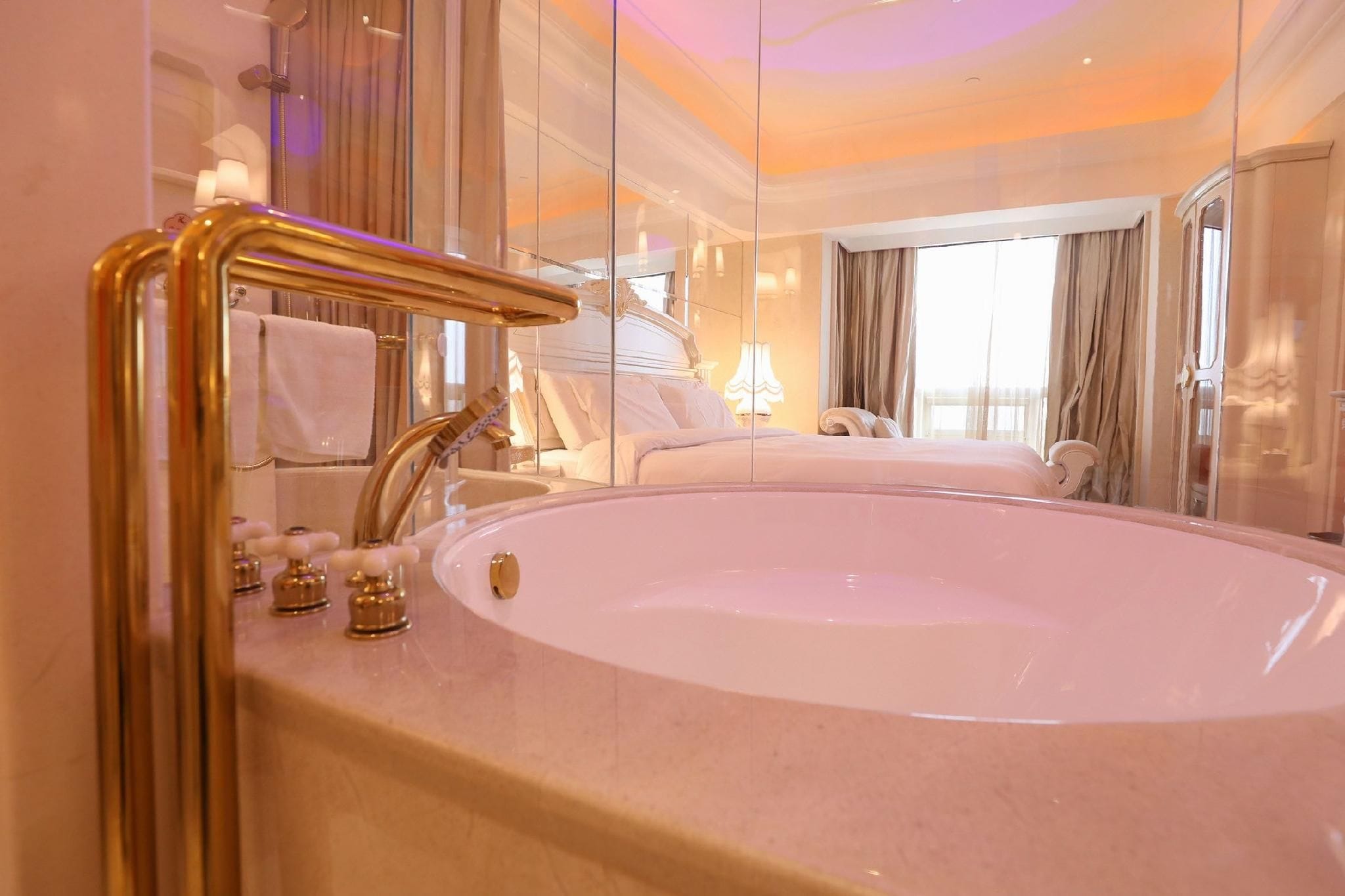 A luxurious bathroom with a large oval bathtub, a gold faucet, and a mirror reflecting the room.