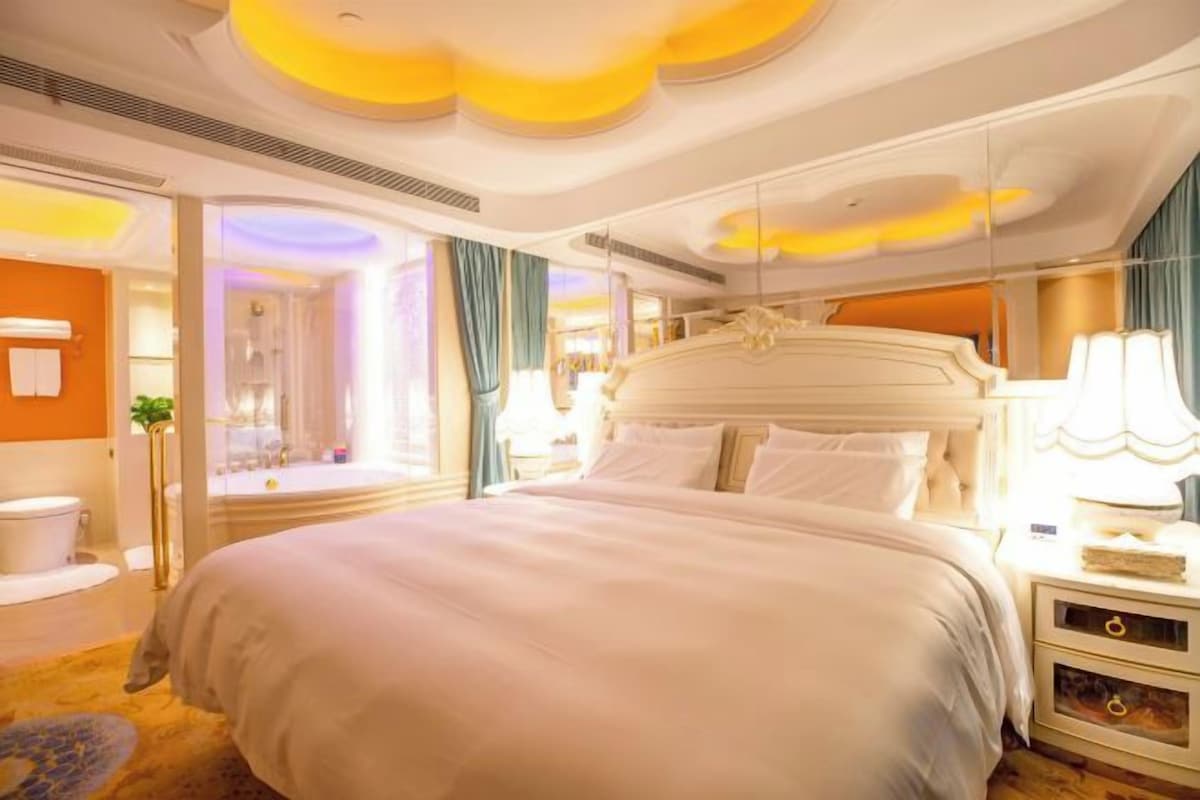 A hotel room with a large bed, a bedside table, a lamp, and a view of the bathroom.