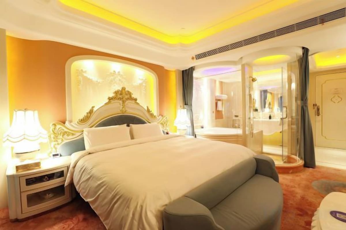A hotel room with a large bed, bedside tables, a mirror, and a bathroom visible through a glass door.