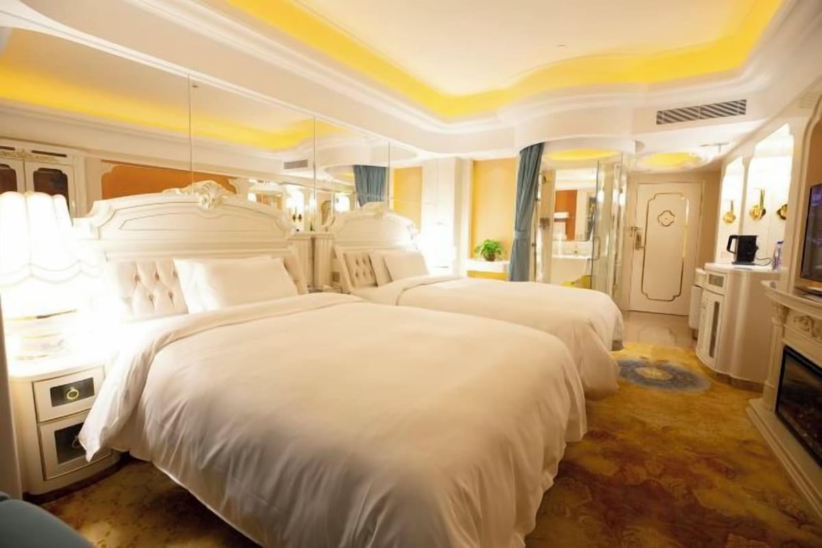 A hotel room with two beds, a sitting area, a fireplace, and a mirror.