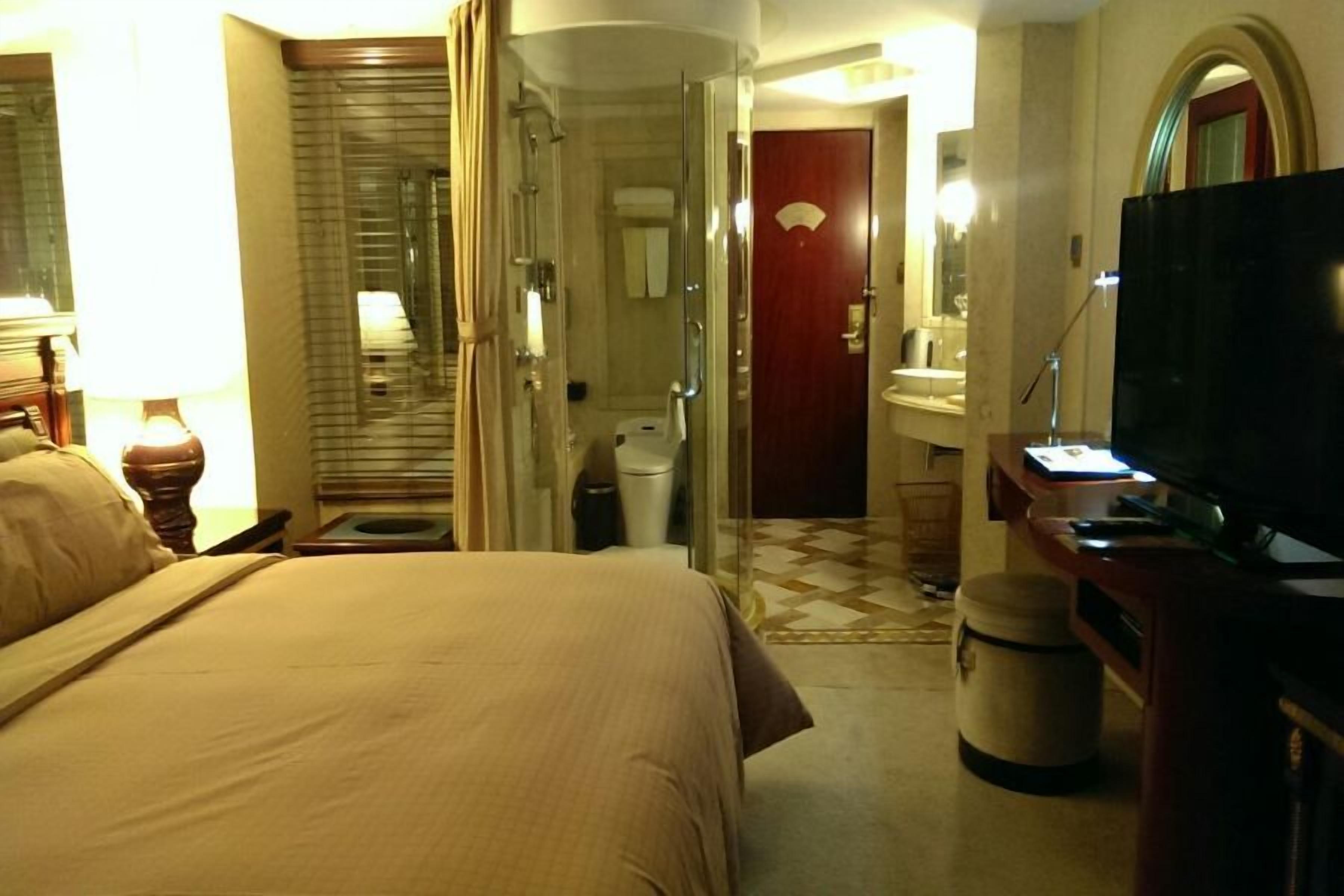 Een hotelkamer met een bed, een televisie, een badkamer met douche en een klein bureau met lamp.