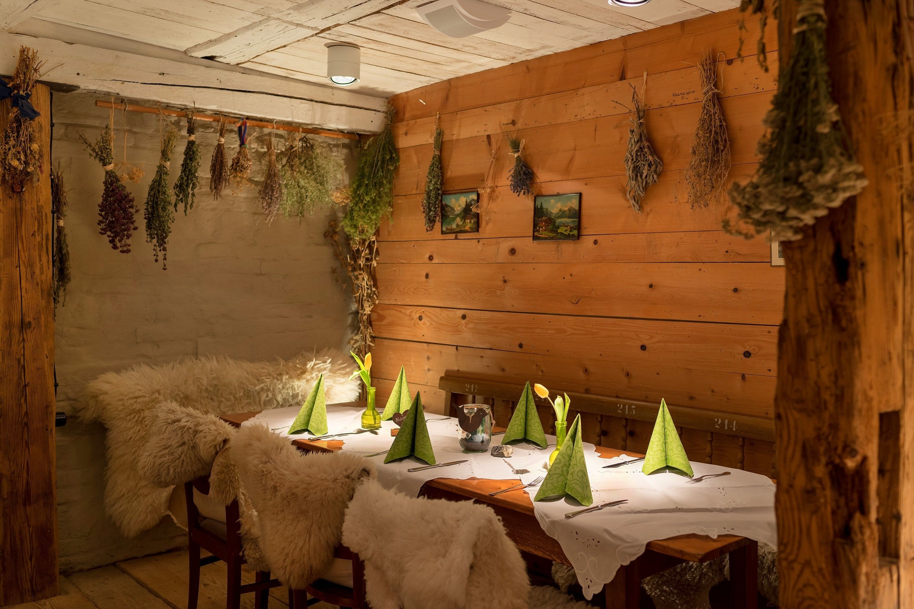 A rustic dining area with wooden walls, hanging herbs, and a white tablecloth.