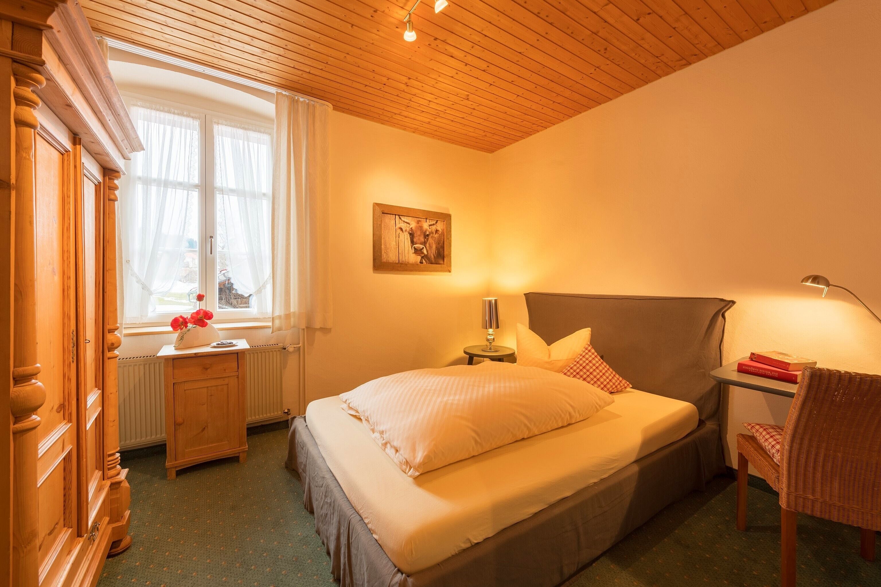 Um quarto aconchegante com cama, mesa de cabeceira, luminária, cadeira e janela com cortinas.
