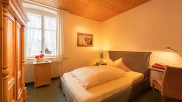 Um quarto aconchegante com cama, mesa de cabeceira, luminária, cadeira e janela com cortinas.