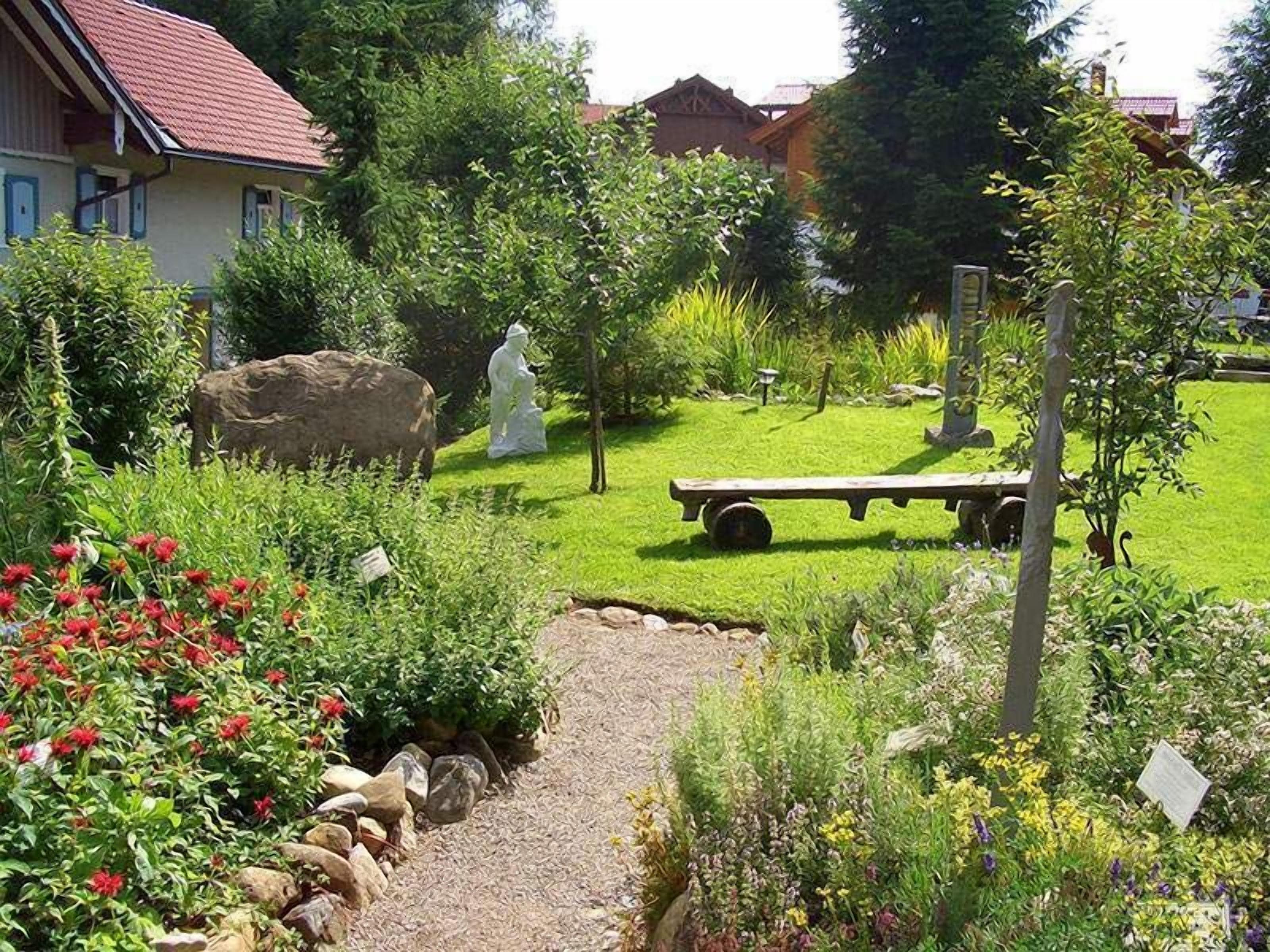A garden with a gravel path, various plants, a white statue, and a wooden bench.