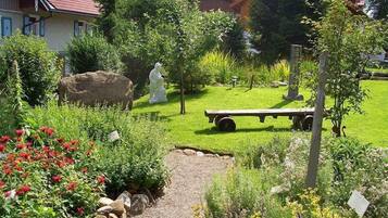 A garden with a gravel path, various plants, a white statue, and a wooden bench.