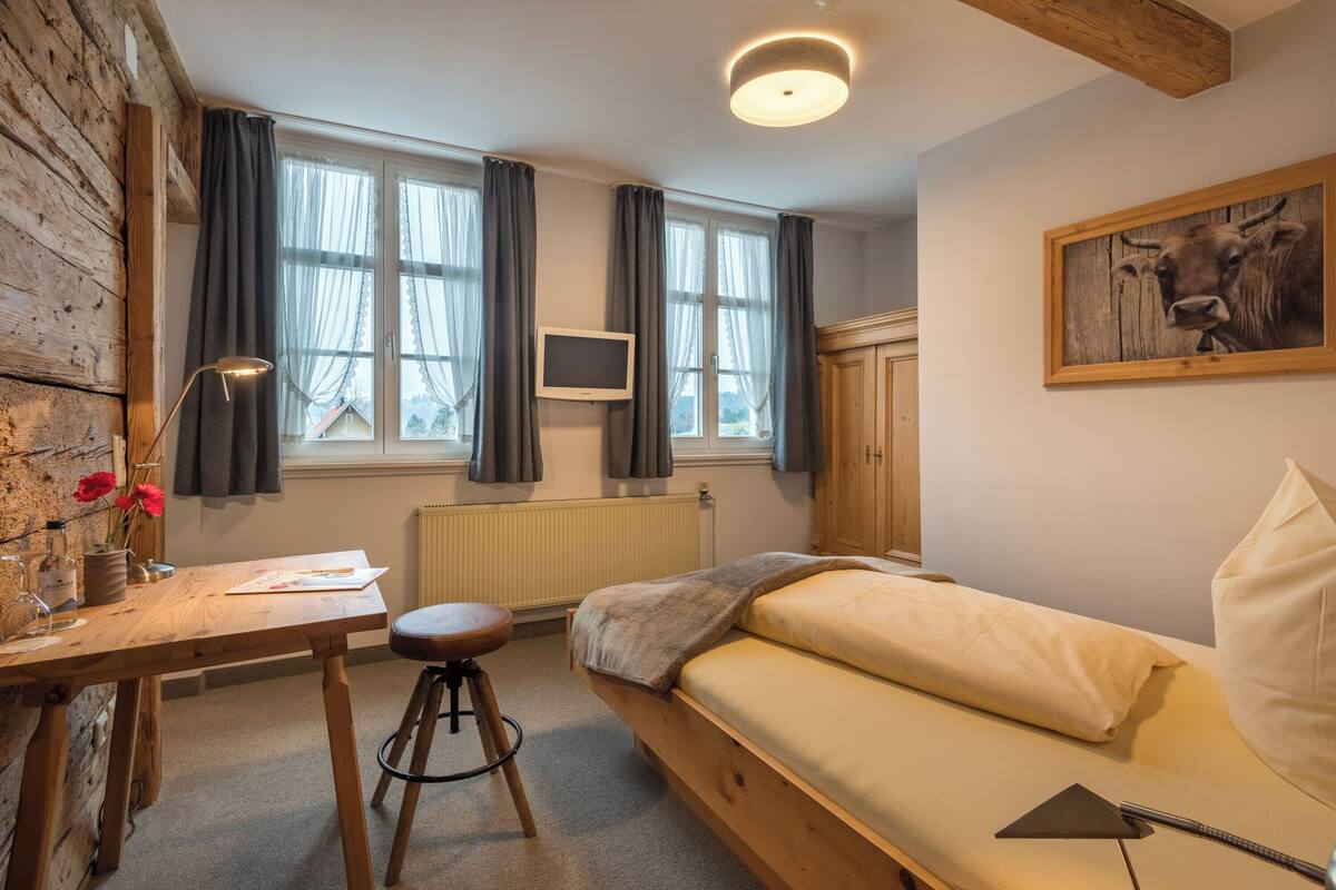 Une chambre confortable avec un lit en bois, un bureau avec une lampe, un radiateur et un téléviseur fixé au mur.