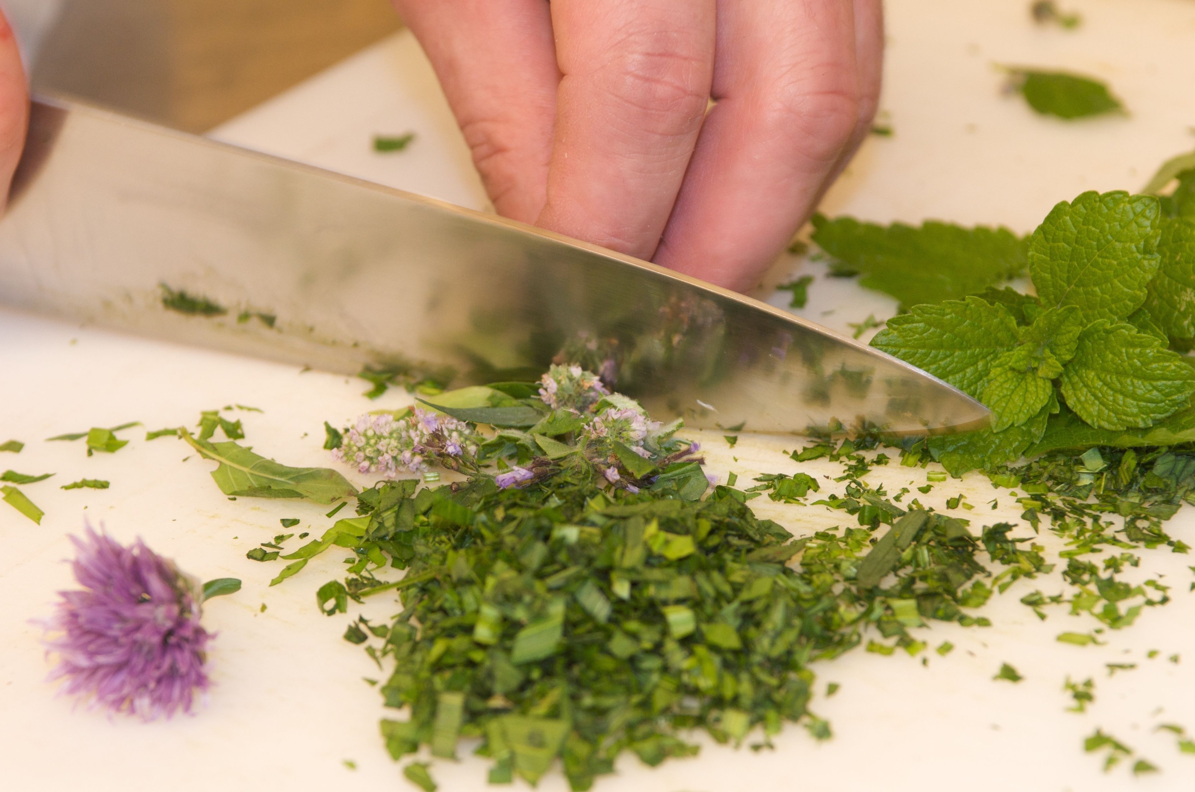 A person chopping herbs on a white cutting board.
