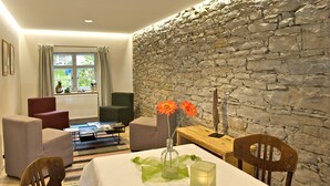 A cozy room with a stone wall, a dining table with chairs, and a comfortable seating area with sofas and a coffee table. - Landgasthof Rössle - Beim Kräuterwirt (Stiefenhofen)