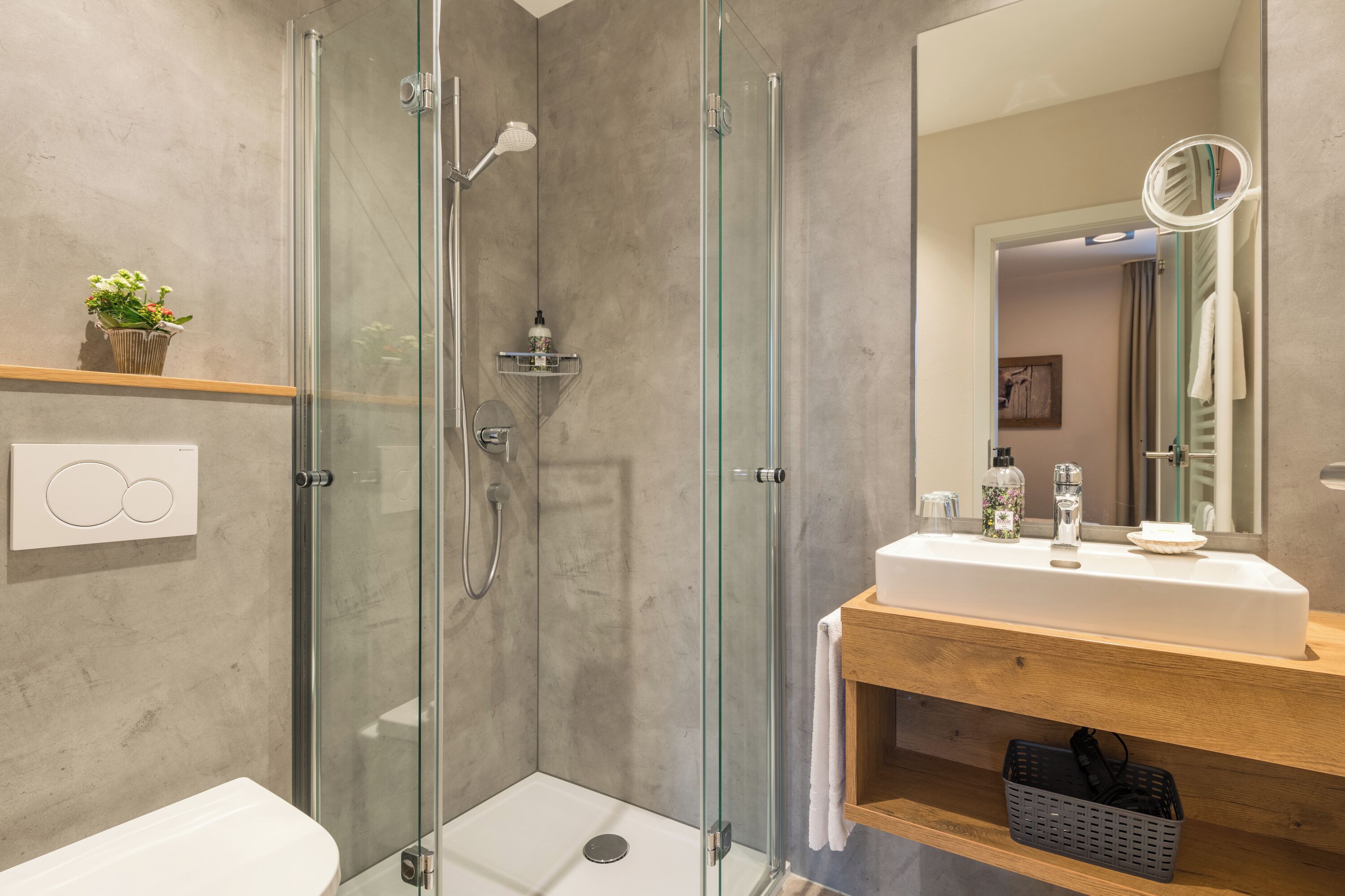 A modern bathroom with a glass-enclosed shower, a wooden vanity with a mirror, and a white sink.