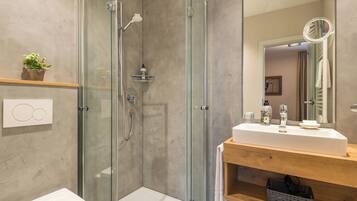 A modern bathroom with a glass-enclosed shower, a wooden vanity with a mirror, and a white sink.