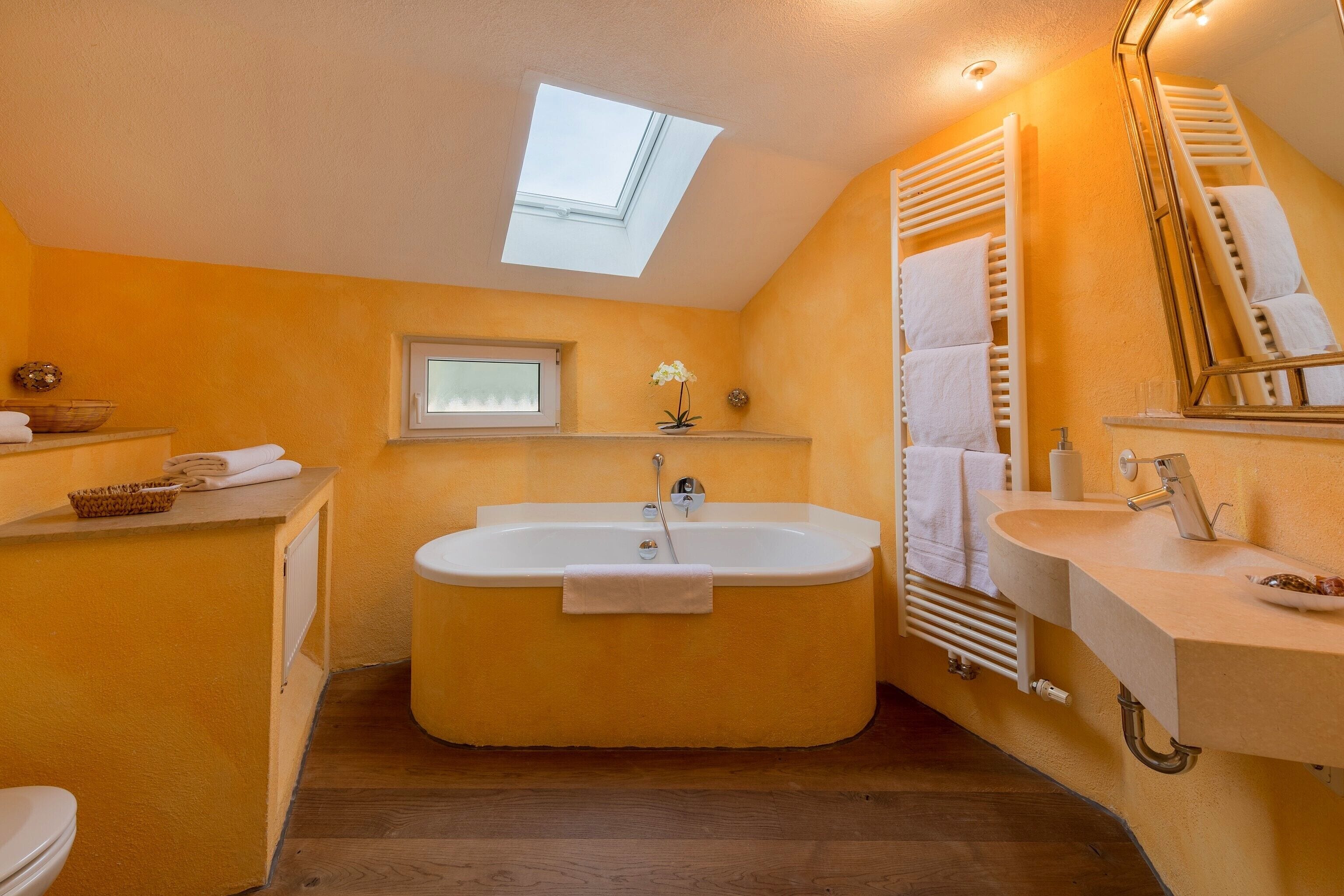 A bathroom with a skylight, a bathtub, a sink, and a mirror.
