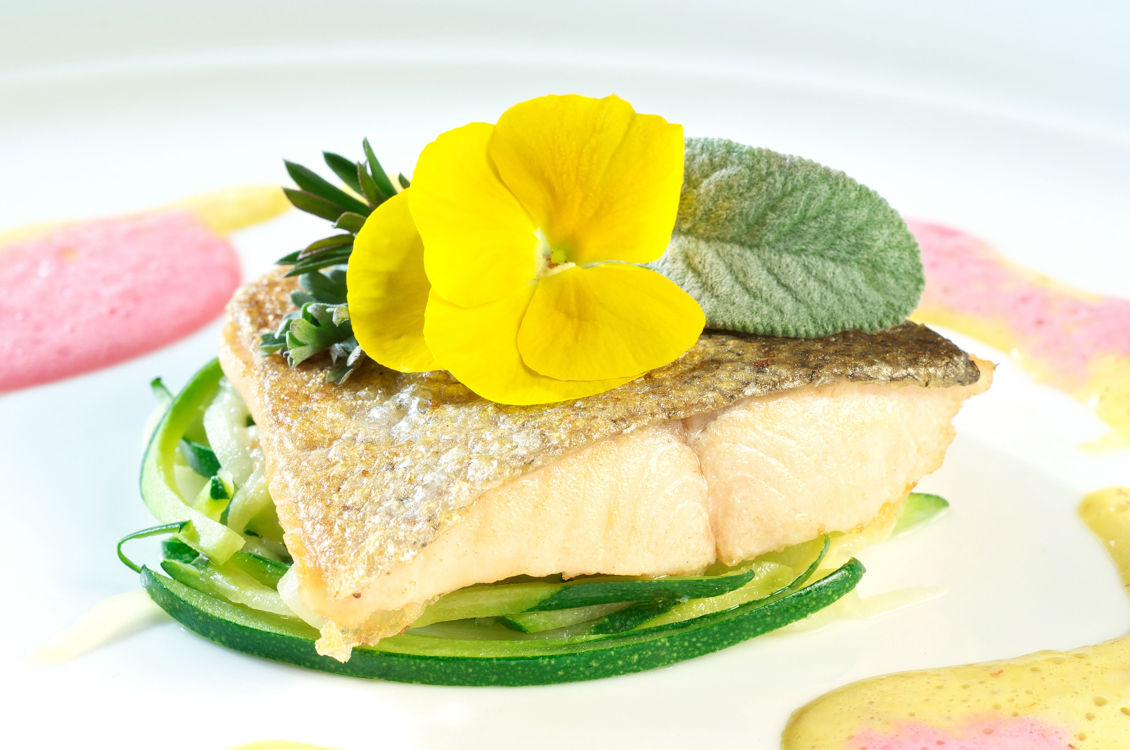 A dish with fish, green vegetables, and yellow flowers.