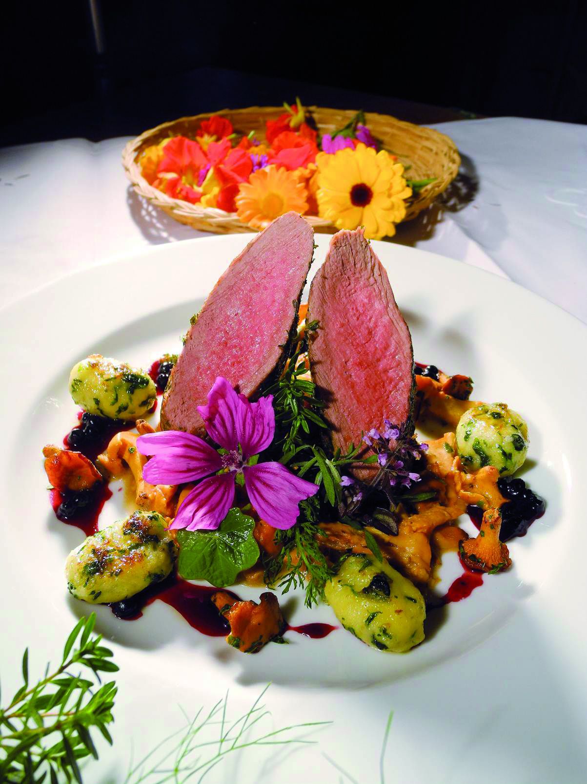 A plate of food with a pink center, surrounded by various vegetables and garnished with flowers.