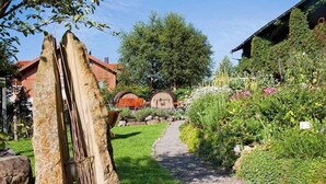A garden pathway leading to a rustic building with a red roof, surrounded by lush greenery and a variety of plants. - Landgasthof Rössle - Beim Kräuterwirt (Stiefenhofen)