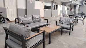 Un área de estar exterior moderna con sofás grises y mesas, una silla de ruedas y un balcón con barandillas.