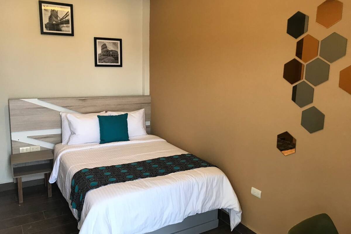 Una habitación de hotel con cama, mesita de noche, silla y decoración hexagonal en la pared.