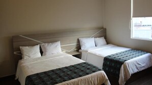 Habitación de hotel con dos camas, cada una con cabecero, ropa de cama blanca y una colcha estampada.