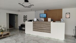 Zona de recepción de un hotel con piso de mármol, mostrador de madera, televisor montado y un certificado enmarcado en la pared.