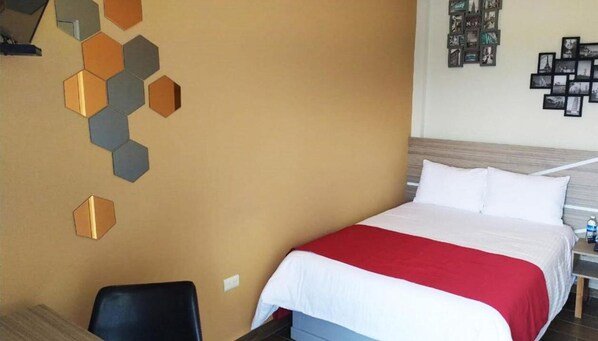 A hotel room with a bed, a desk, and a chair. There is a wall decoration with hexagonal shapes.